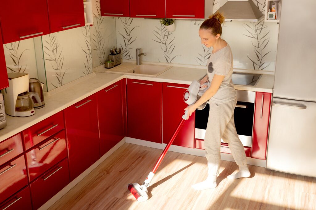 Young woman vacuums the floor in the kitchen